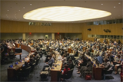 [ai] A large audience gathered in a formal conference room, seated in rows with desks. The room is well-lit, featuring a circular ceiling and wooden paneling, indicating a significant meeting or event.